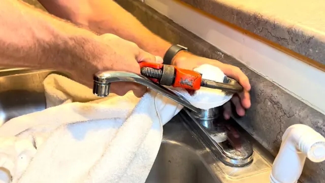 Hands using a wrench wrapped in a towel to remove a kitchen faucet